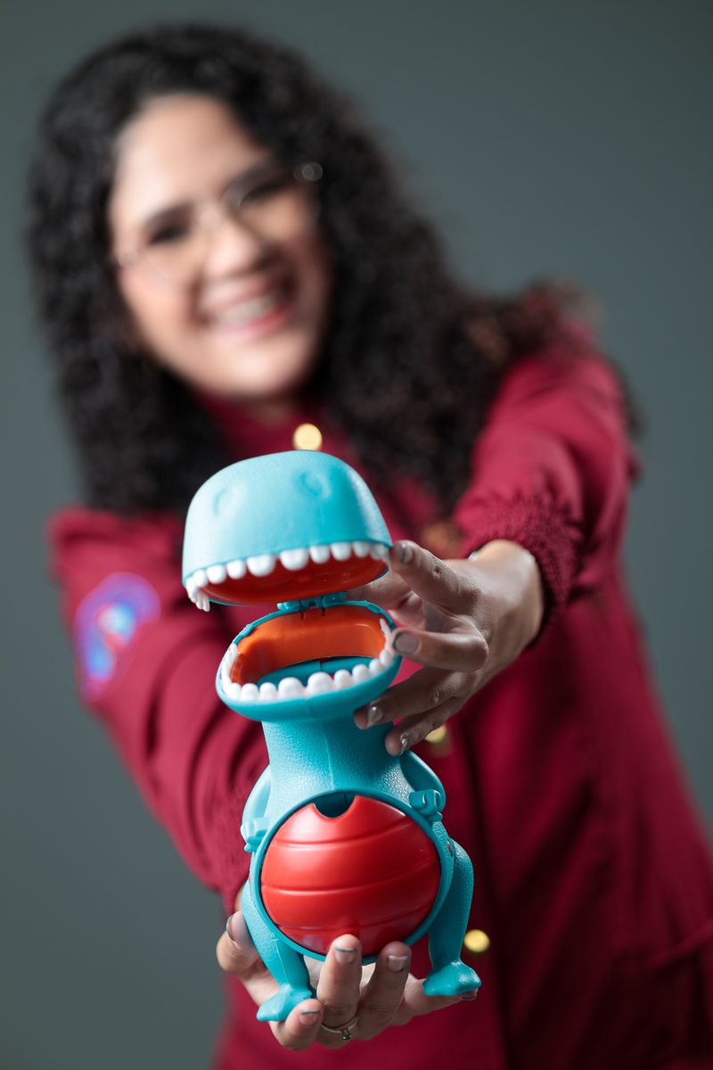 Gabrielle Aquino estendendo um brinquedo de dinossauro em direção à câmera, com foco no brinquedo.