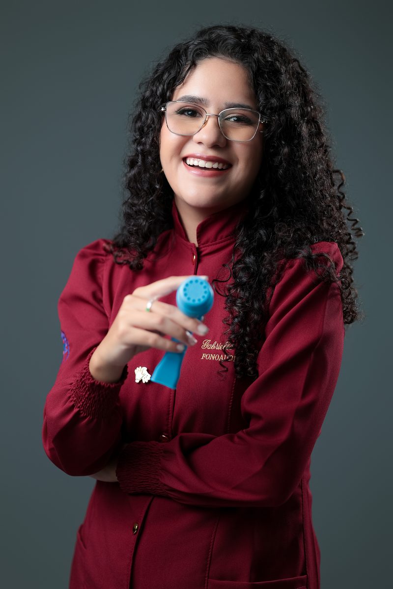 Gabrielle Aquino sorrindo, segurando um massageador facial usado em terapia vocal.